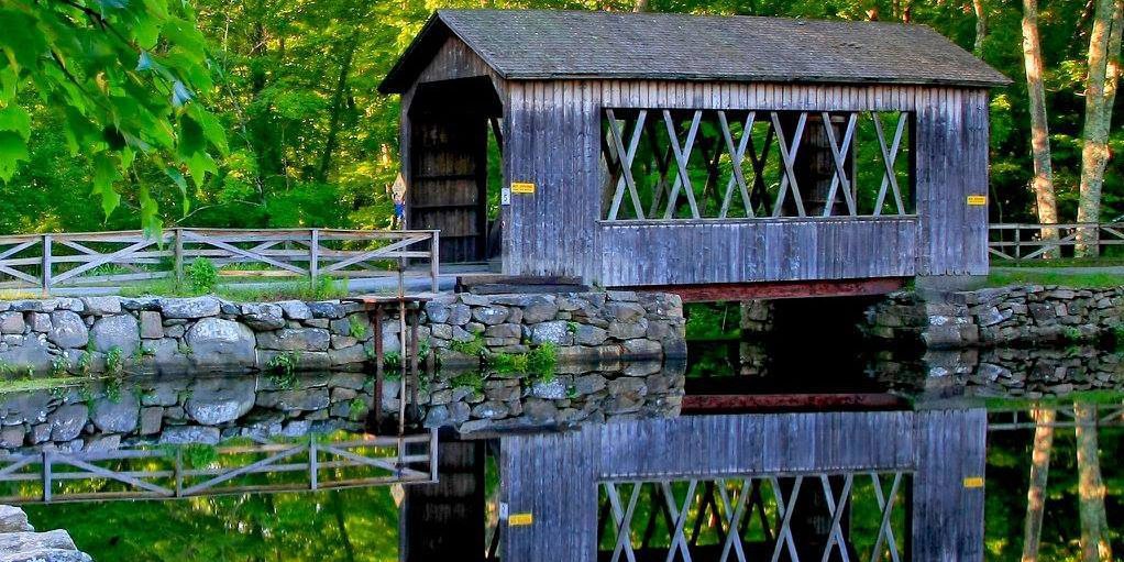 Covered Bridge at Sutton Falls Campground in Sutton, Massachusetts Covered bridge at Sutton Falls Campground reflected in calm water on a summer day