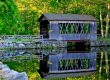 Covered bridge at Sutton Falls Campground reflected in calm water on a summer day